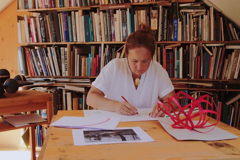 Žena sedí pri stole s knihami a navrhuje projekt