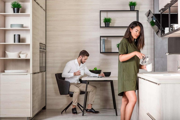 Svetlá kuchyňa s mužom pri stole a ženou, ktorá pripravuje kávu