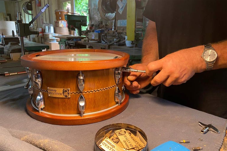Muž ladí drevený bubon s chrómovaným kovaním a logom Hallvad Drums.