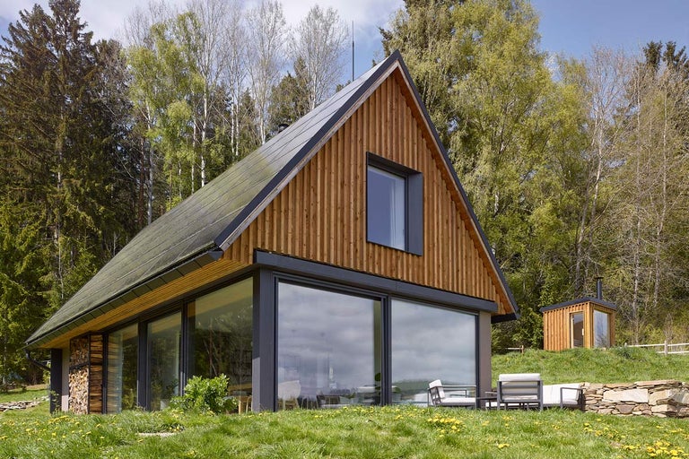 Moderný drevený dom so solárnymi panelmi na streche a veľkými oknami vo vidieckom prostredí