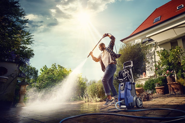 Muž čistí terasu vysokotlakovým čističom vonku.