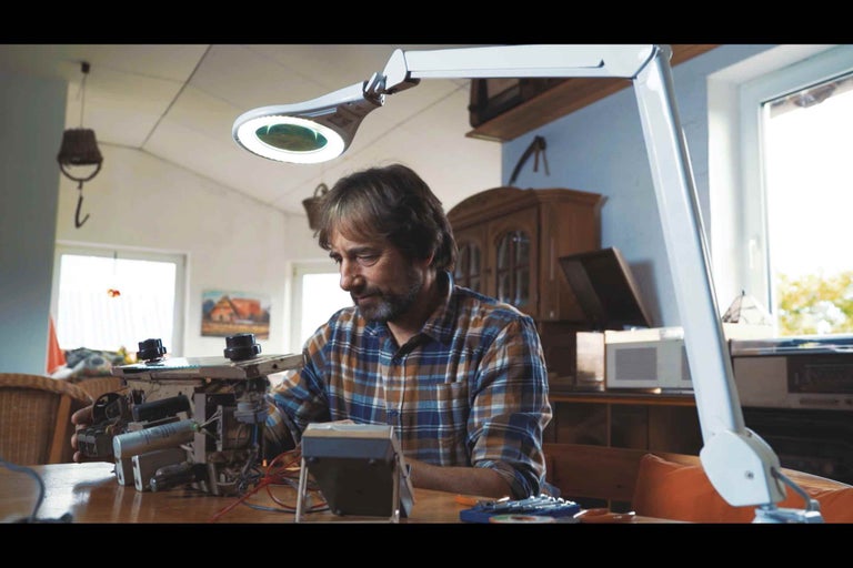 Muž pracuje s lupou na elektronických súčiastkach na stole.