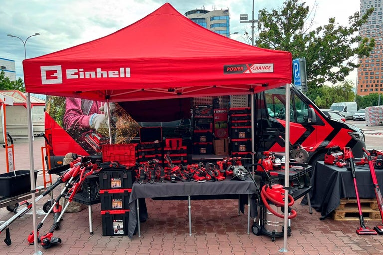 Vonkajší stánok s výberom náradia Einhell pod červeným stanom.