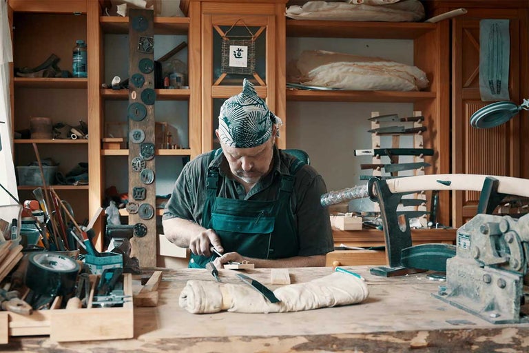 Remeselník pracuje s nástrojmi v dielni s regálmi.