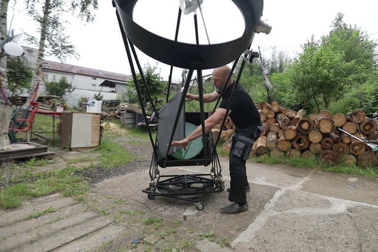 Muž montuje veľký astronomický teleskop vonku.