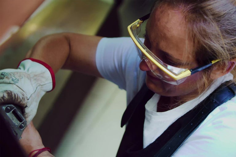 Žena s ochrannými okuliarmi a pracovnými rukavicami pri práci.