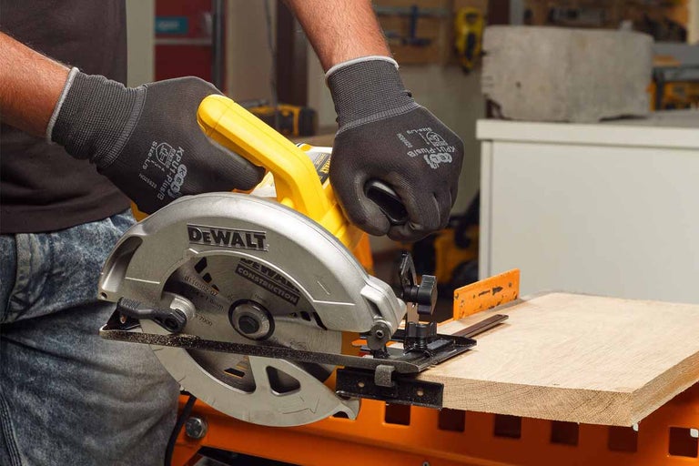 Ručná kotúčová píla DeWalt reže drevenú dosku, pričom sú nosené pracovné rukavice.