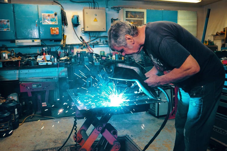 Muž zvára kov v dielni so zváračkou na ponku