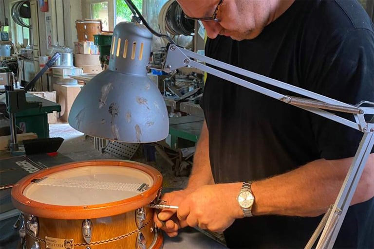 Remeselník pracujúci na drevenom bubne pod stolnou lampou.