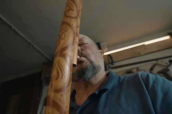 Muž hrá na zdobené didgeridoo.
