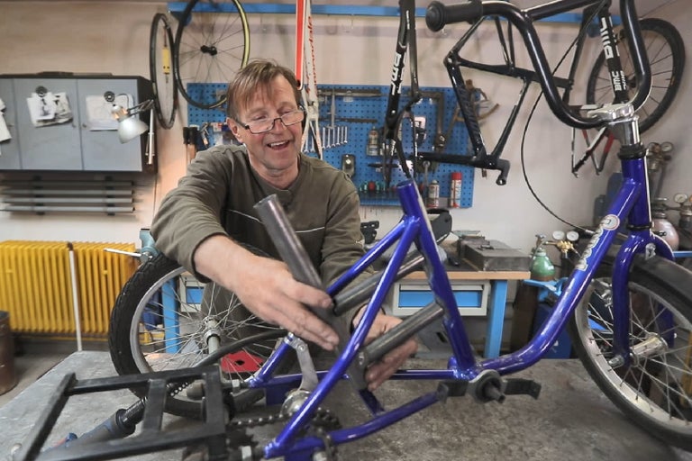 Muž montuje modrý bicykel v dielni.