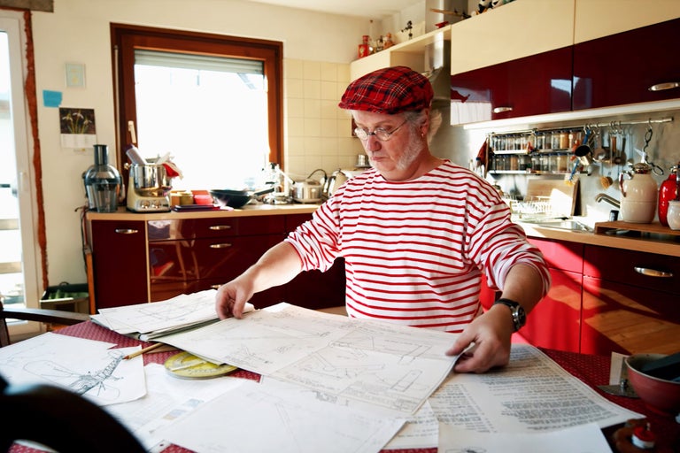 Muž si prezerá stavebný plán v kuchyni s kuchynskými spotrebičmi a skriňami