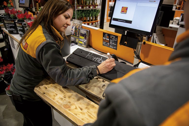 Zamestnankyňa píše na drevenú tabuľu nápis Hornbach pri samoobslužnej pokladni
