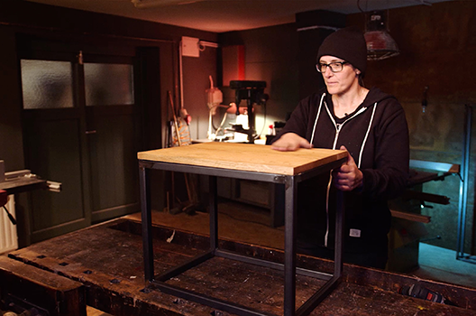 Žena v dielni s dreveným stolom a kovovým rámom