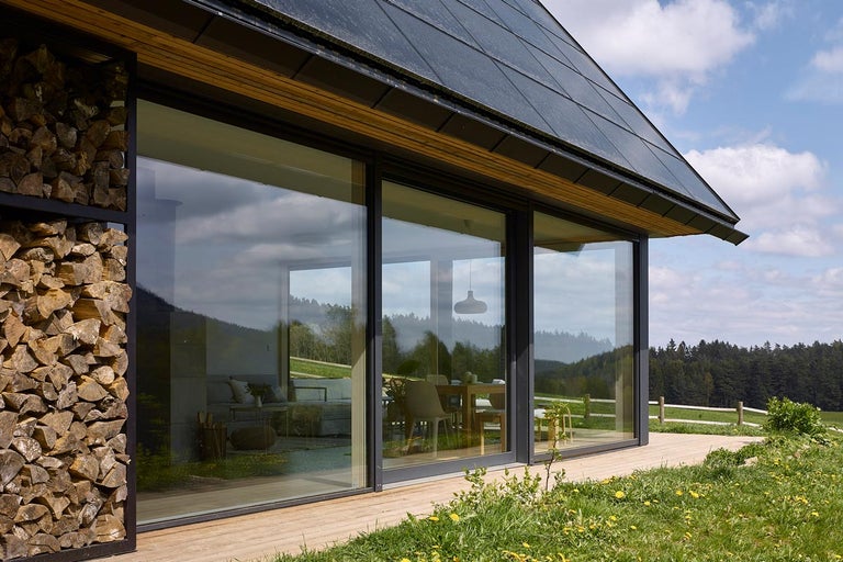 Moderný dom so sklenenou fasádou, hromadou dreva a solárnou strechou