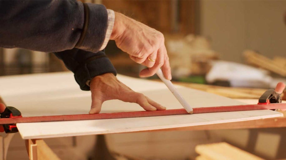 Osoba označuje čiaru ceruzkou a pravítkom na drevenej doske upevnenej svorkami.