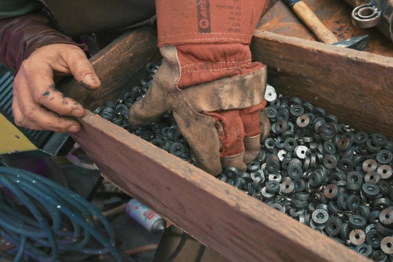 Ruka v pracovnej rukavici siaha do debny s kovovými kotúčmi.