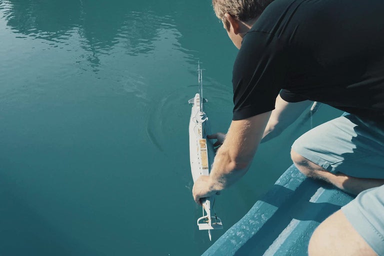 Muž spúšťa diaľkovo ovládanú ponorku do vody.