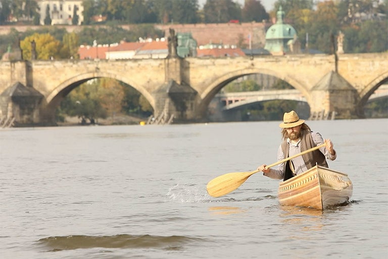 Muž vesluje na kanoe na rieke pred Karlovým mostom