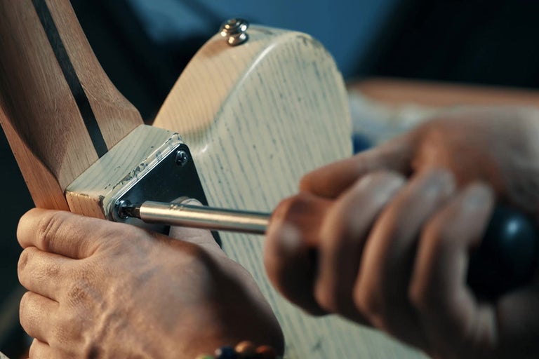 Osoba pripevňuje krk elektrickej gitary k telu pomocou skrutkovača.