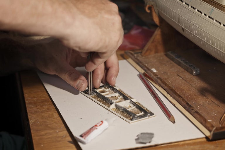 Osoba montuje model lode pomocou pinzety a lepidla.