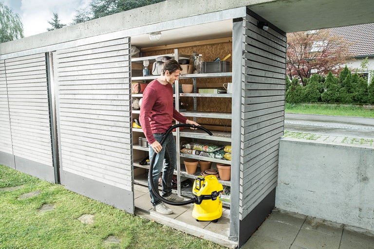 Muž vysáva skladovací regál viacúčelovým vysávačom v záhradnom domčeku
