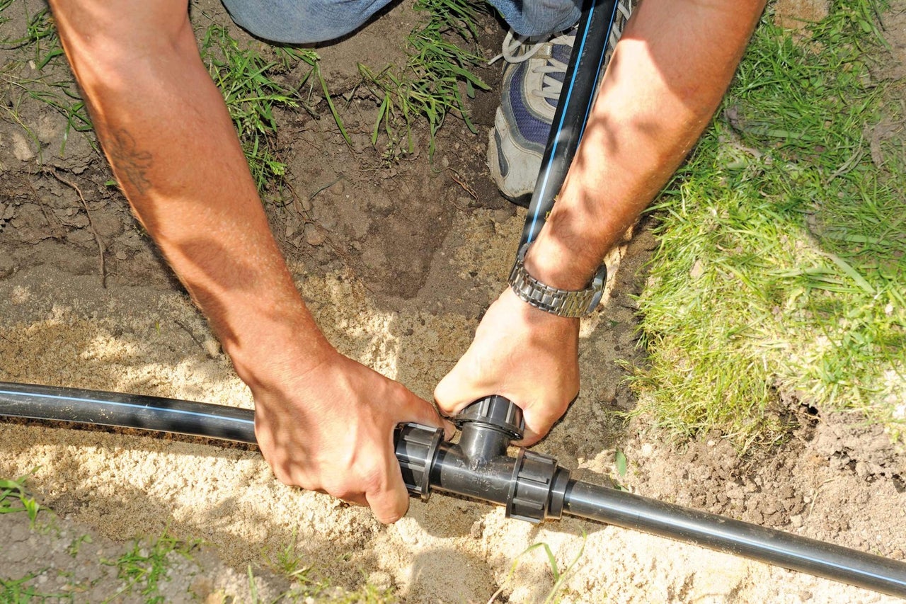 Inštalácia zavlažovacieho systému s čiernou plastovou rúrkou a T-spojkou v záhrade.