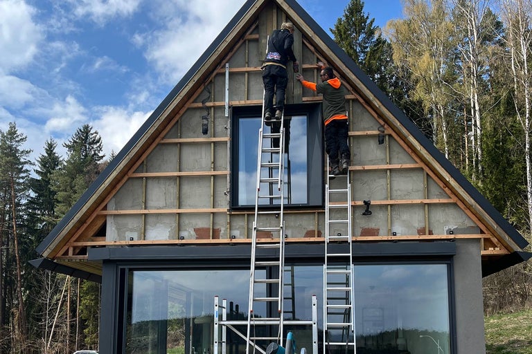 Dvaja remeselníci na rebríkoch montujú fasádu na dom.
