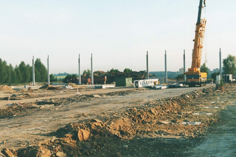 Stavenisko so žeriavom, betónovými piliermi a stavebnými materiálmi