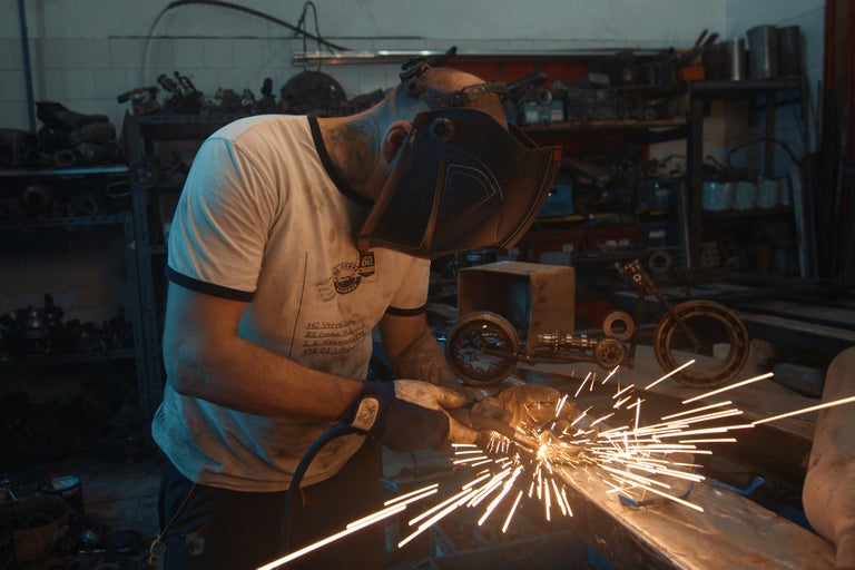 Muž s ochrannou maskou zvára kov v dielni