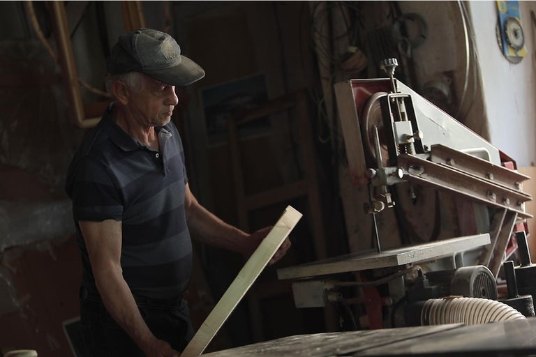 Muž pracuje s pásovou pílou na kuse dreva.