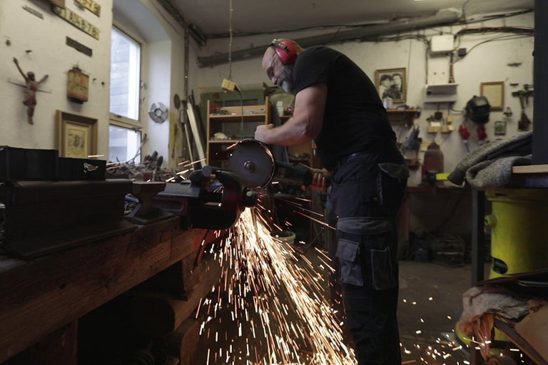 Muž brúsi kov uhlovou brúskou v dielni