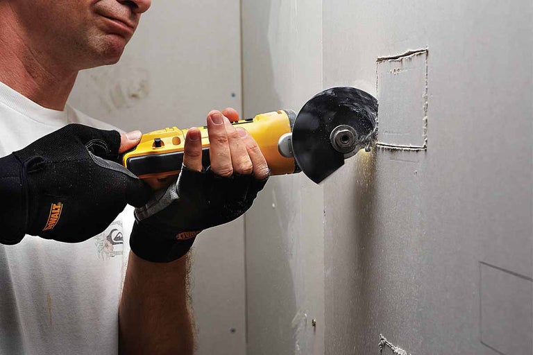 Osoba vyrezáva otvor do sadrokartónu pomocou rozbrusovacej píly.