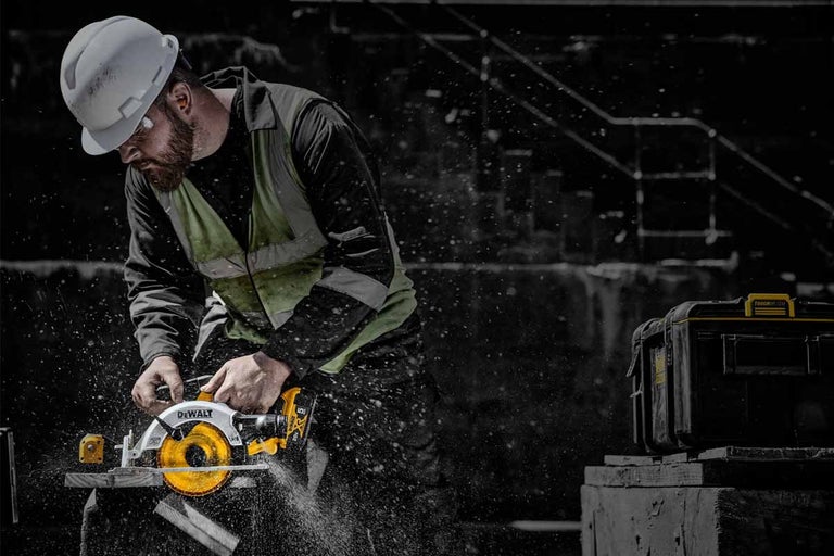 Stavebný robotník reže drevo ručnou kotúčovou pílou DeWalt, v pozadí je box na náradie.