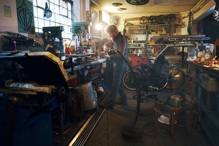 Dielňa s náradím, pracovným stolom, bicyklami a osobou pracujúcou na projekte.