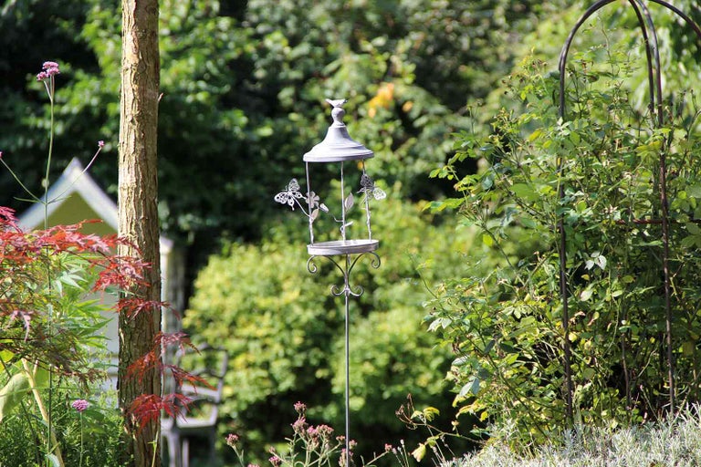 Dekoratívne napájadlo pre vtáky s motýľovým dizajnom v záhrade.