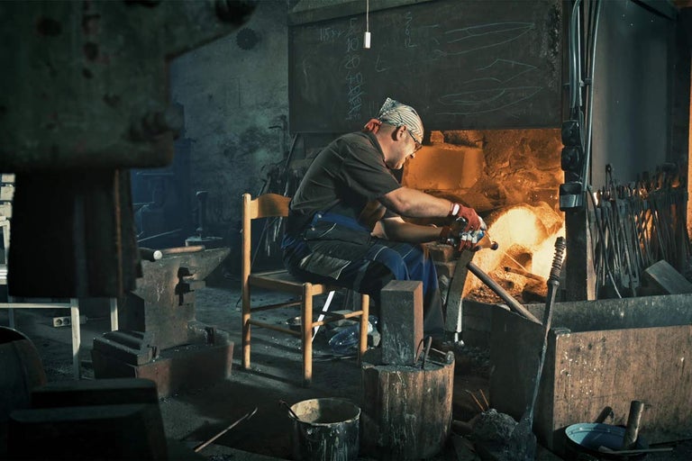 Kováč spracováva kov v dielni s nákovou a vyhňou