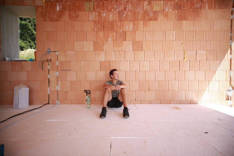 Interiérový záber hrubej stavby s tehlovými stenami a izolovanou podlahou, na ktorej sedí muž