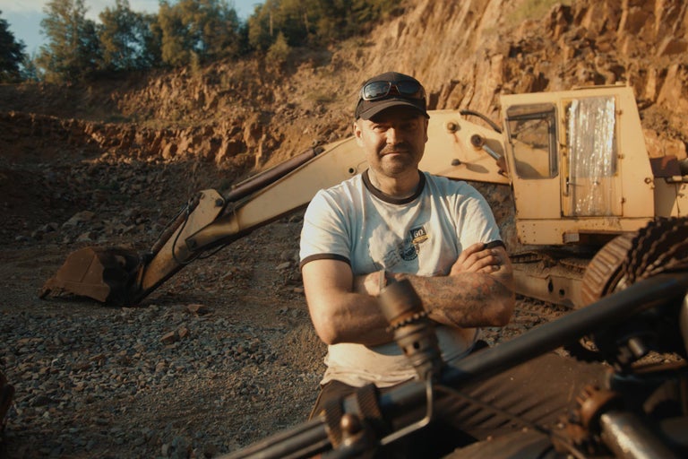 Muž stojí pred bagrom v kameňolome.