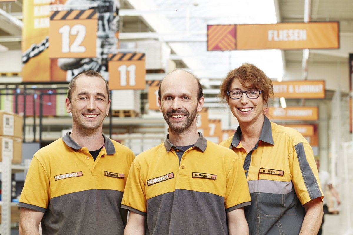 Traja zamestnanci Hornbach v pracovnom odeve pred regálmi so stavebným materiálom.