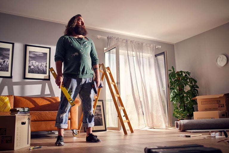 Svetlá miestnosť počas renovácie s remeselníkom, vodováhou, rebríkom a sťahovacími krabicami