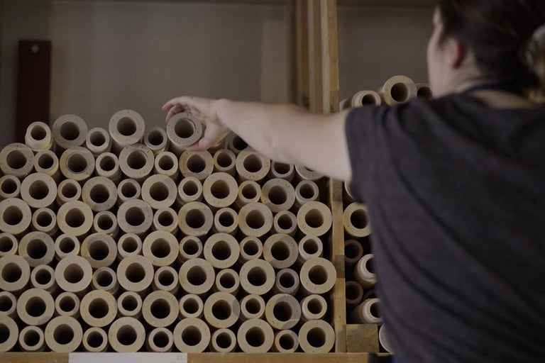 Záber okrúhlych drevených dištančných prvkov naskladaných v regáli, pričom jedna osoba dištančný prvok vyberá.