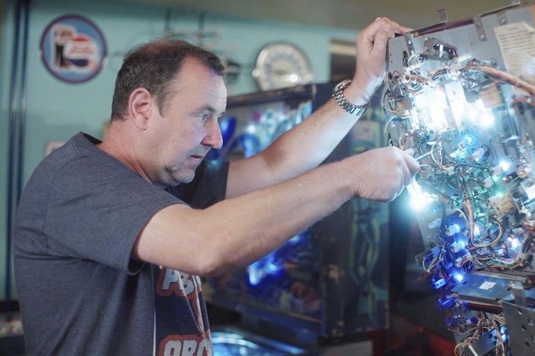 Muž opravuje flipper s drôtmi a žiarovkami.
