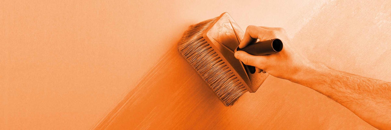 Osoba nanáša lazúrovací štetec na stenu