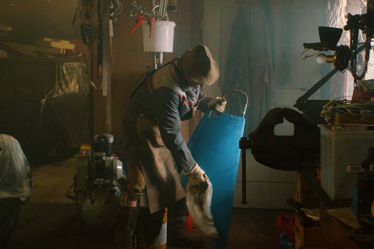 Dielňa s osobou, ktorá čistí modrú kovovú dosku, obklopenou náradím a vybavením.