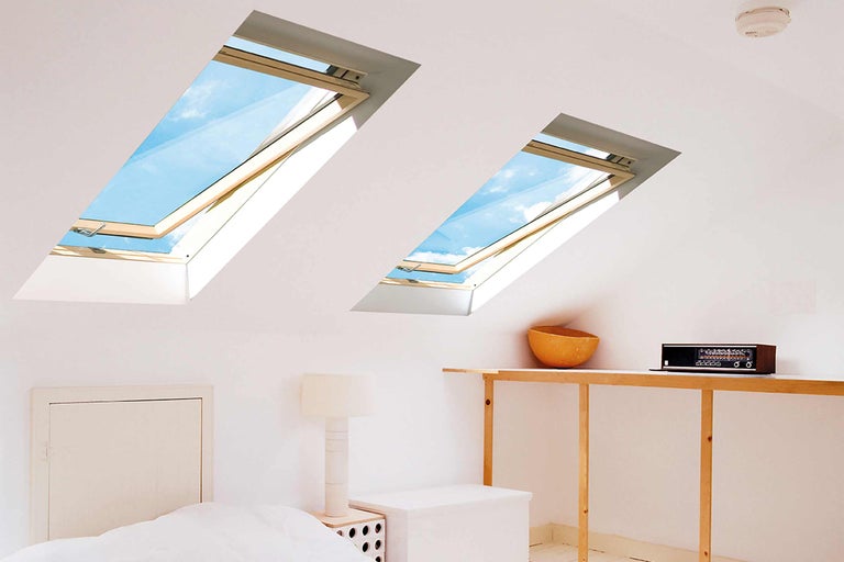 Dve strešné okná osvetľujú podkrovnú izbu s posteľou a nábytkom.