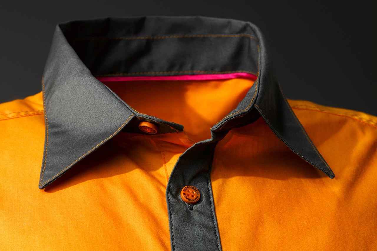Detail oranžovej pracovnej košele so sivým golierom a logom Hornbach na gombíkoch.