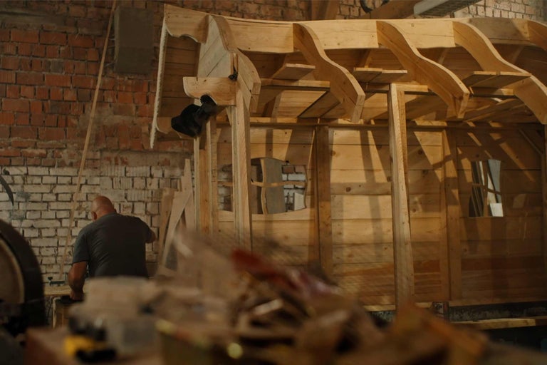 Nedokončený drevený dom v hrubej stavbe s pracovníkom v pozadí.