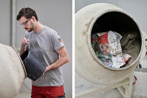 Muž s ochrannými okuliarmi leje obsah z vedra do miešačky na betón