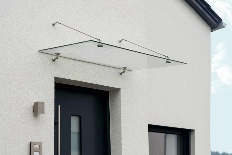 Sklenený baldachýn nad vchodovými dverami s nerezovými držiakmi na stene domu